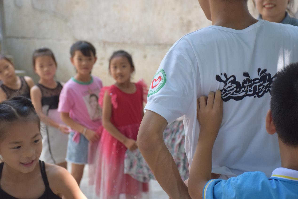 下课时间志愿者与孩子们玩游戏，一个孩子调皮地跑到志愿者的身后揪住志愿者衣服